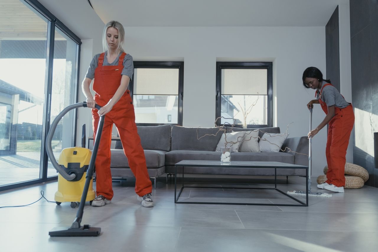 Crafting Captivating Headlines: Your awesome post title goes here Two women in red overalls vacuuming and sweeping a modern living room.
